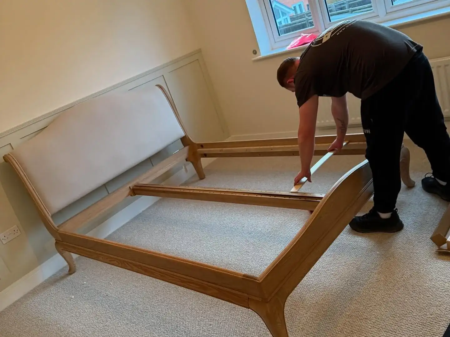 A Wolves Removals crew member assembling a new oak sleigh bed frame in a bedroom during a house move