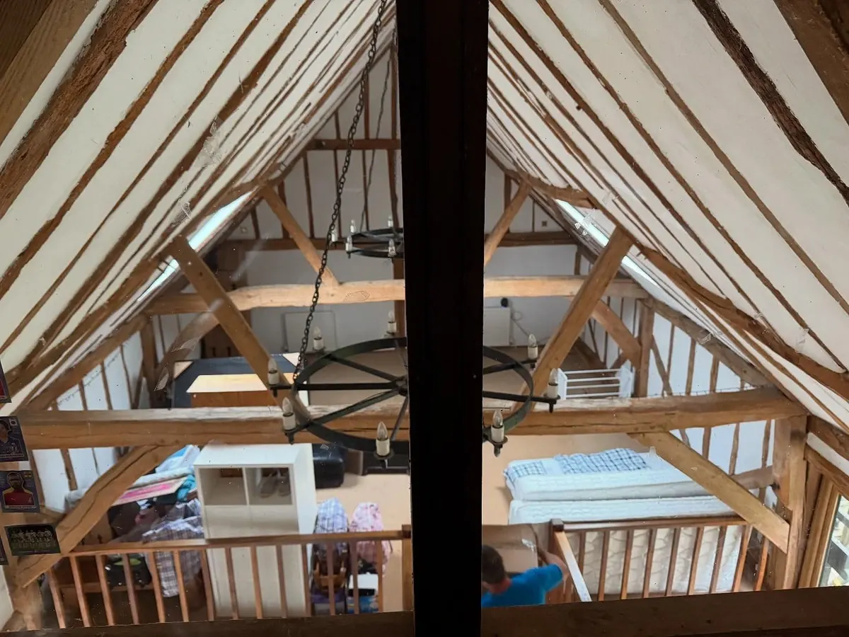 A galleried bedroom under the exposed oak roof trusses of a period barn conversion