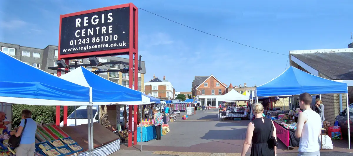 Market stalls under blue gazebos beside the Regis Centre sign in Bognor Regis town centre