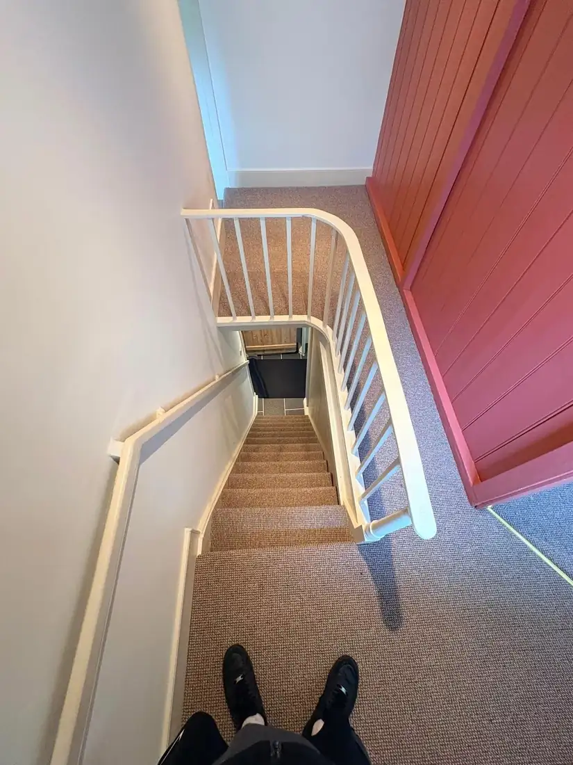 A narrow cottage staircase with a turn and handrail, photographed from the top step