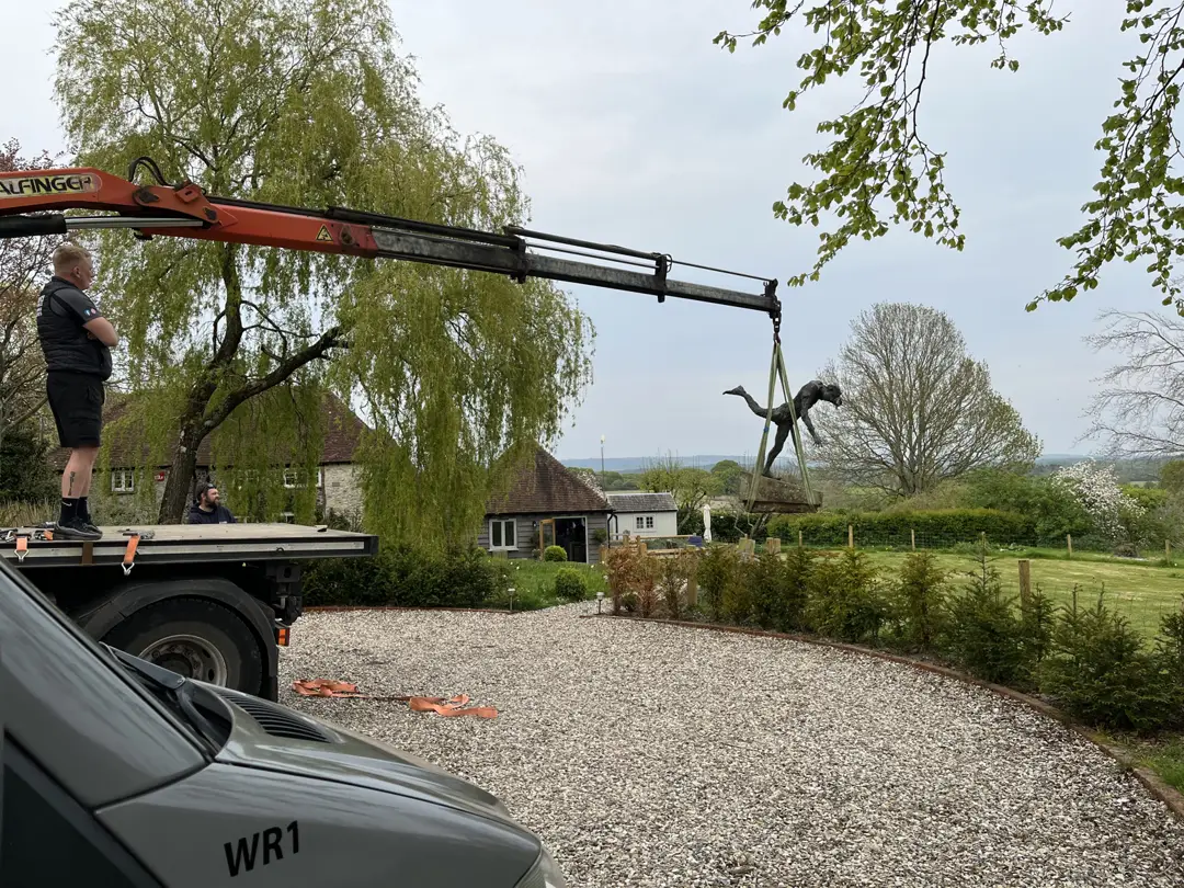 Crane loading a statue onto a trailer in the countryside