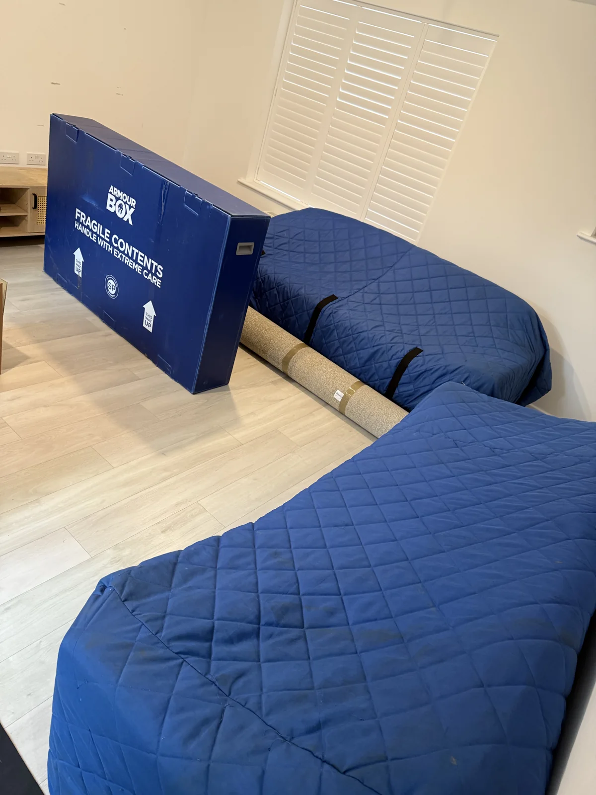Furniture wrapped in blue quilted moving blankets with a fragile-contents box
