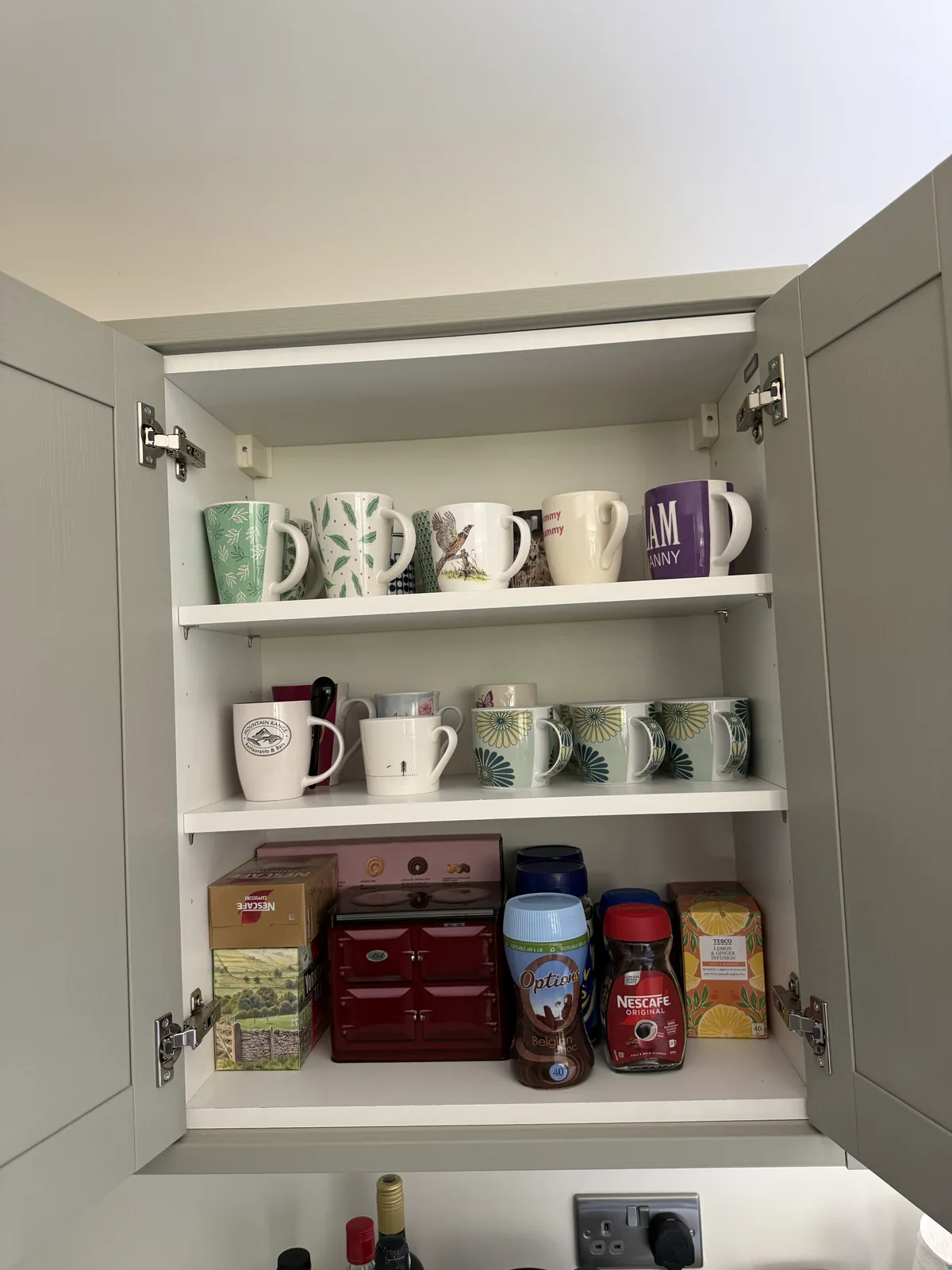 Mugs and tea things arranged on the shelves of a kitchen wall cupboard after unpacking