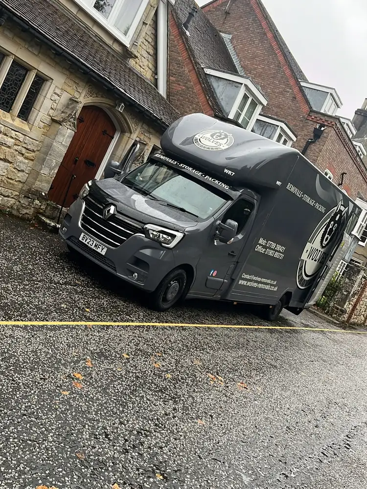 Grey Wolves Removals Luton van on a wet street beside a stone building with an arched wooden door