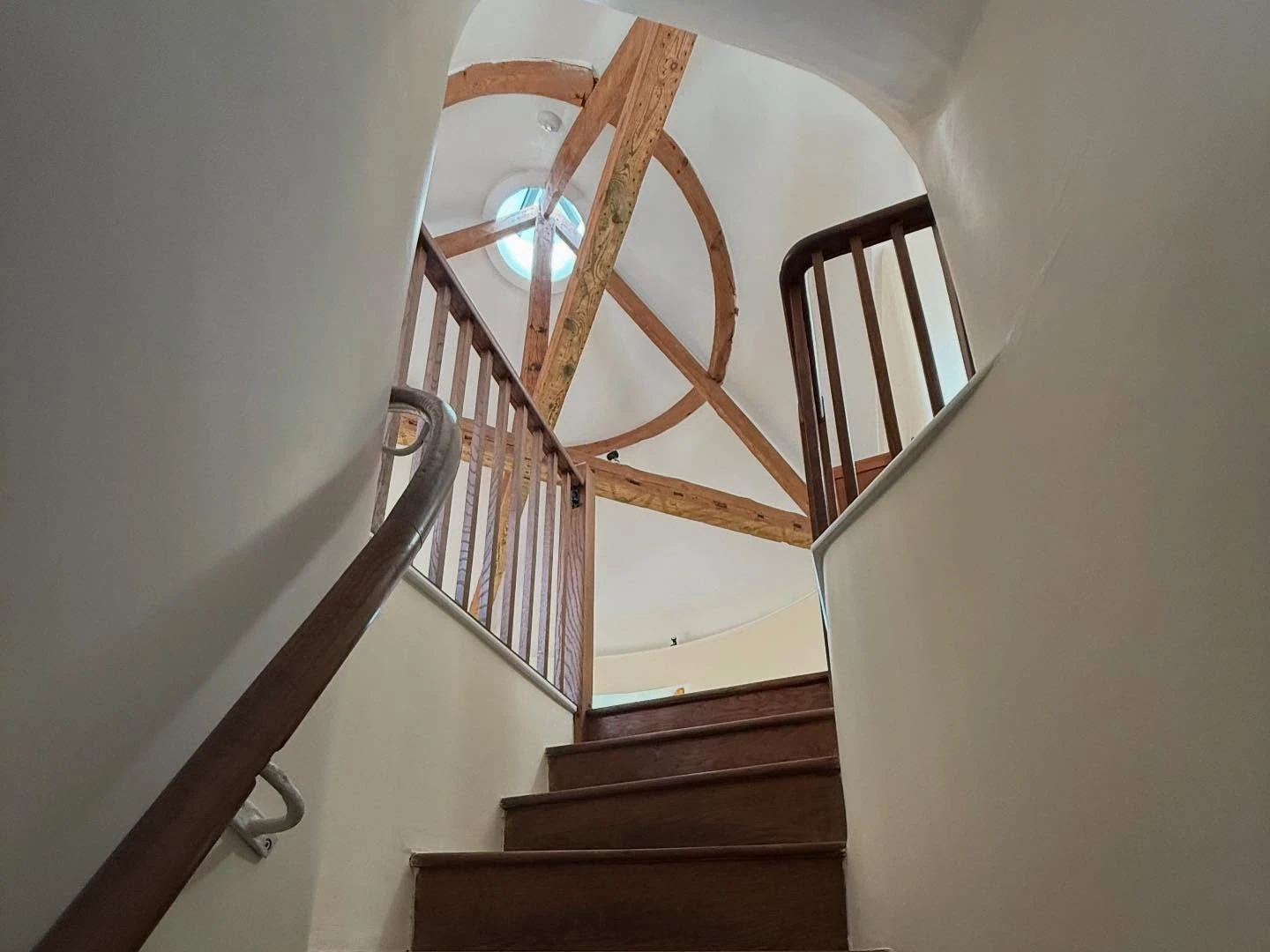 Looking up a curved staircase inside a round house, with exposed roof timbers forming a ring around a circular rooflight
