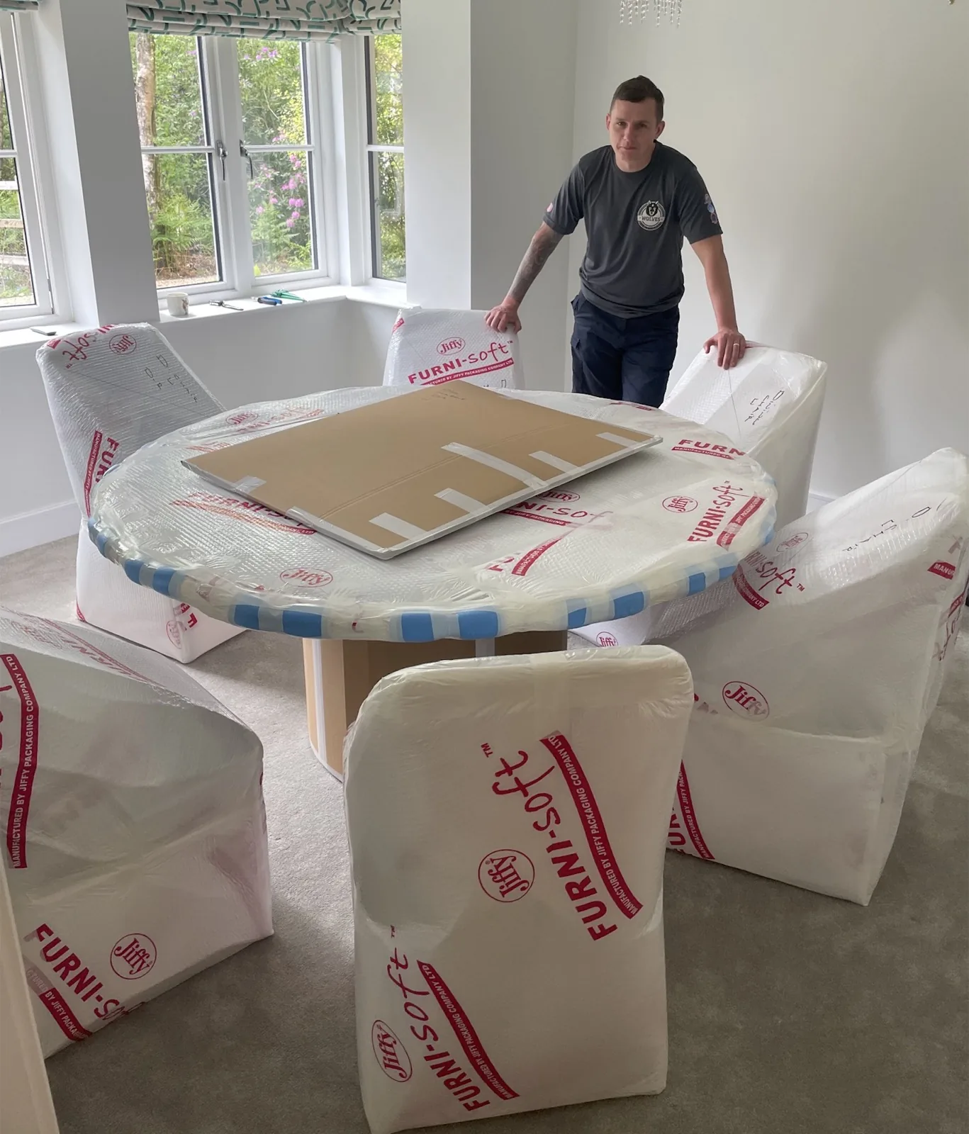 A Wolves Removals mover wrapping a dining table and chairs in protective padding