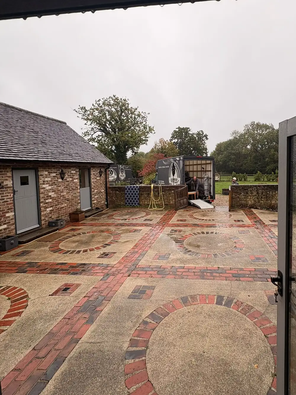Two grey Wolves Removals vans parked beyond the wet brick courtyard at the barn near Haywards Heath, one with its back open and a ramp down