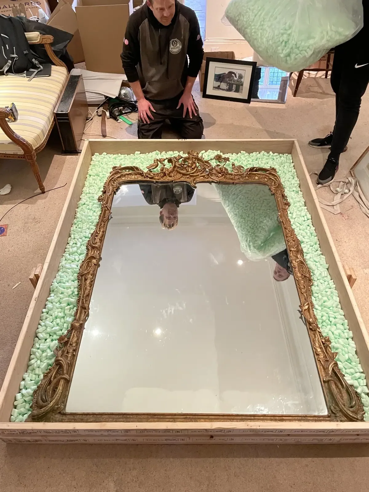 A Wolves Removals packer wrapping an ornate gilt-framed mirror in protective material
